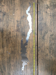 Metal cutout of Lake George with a measuring tape for scale on a wooden surface