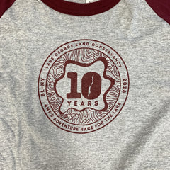 Close-up of a heather gray raglan T-shirt with maroon sleeves and collar trim, featuring a large circular chest graphic that reads '10 YEARS' with Lake George Land Conservancy text around it.