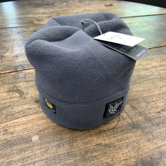 A dark gray fleece beanie hat with a hangtag and a small black brand patch on the front, displayed on a rustic wooden tabletop.